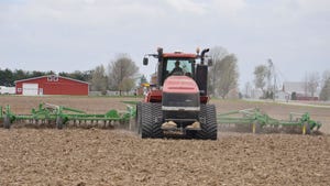 A tractor pulling a tillage implement in a no-till cornfield with a farmstead in the background 