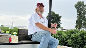 Man sitting on a tour trailer, giving a talk during a farm tour, with fields of cotton in the background.